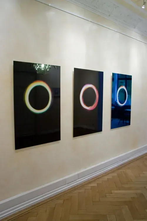 Three of the large prints hung in a row on a pale gallery wall, each a ring on black
